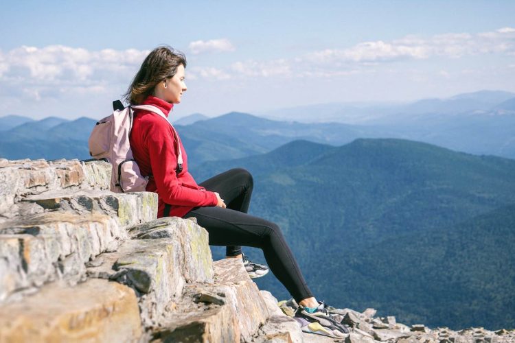 Photo by Levi Kyiv a woman sitting on top of a rock cliff